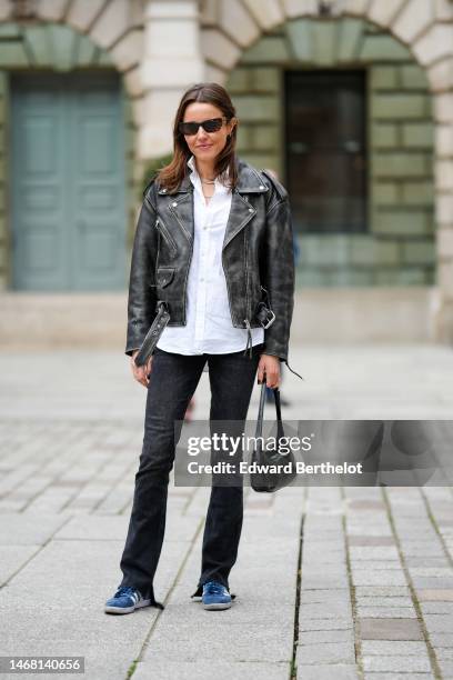 Chloe Street wears black sunglasses, a white shirt, diamonds necklaces, a black faded leather zipper jacket, black denim flared pants, a black shiny...