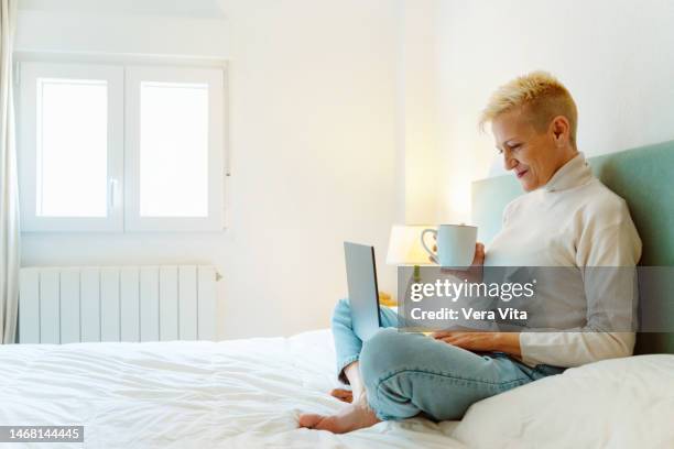 portrait of aged woman using computer learning new technologies at linen bedroom - vita domestica fotografías e imágenes de stock