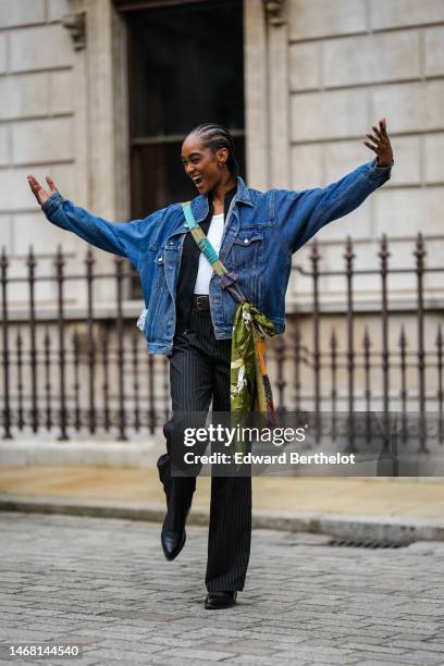 Model wears a white t-shirt, a navy blue denim jacket, a black shirt, a green / purple / blue / orange print pattern silk crossbody bag, black...