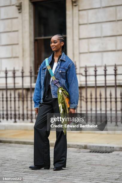 Model wears a white t-shirt, a navy blue denim jacket, a black shirt, a green / purple / blue / orange print pattern silk crossbody bag, black...