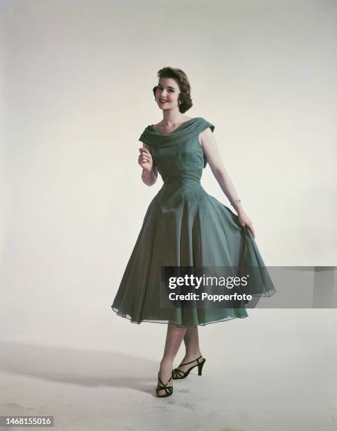 Posed studio portrait of a woman wearing a green chiffon party frock featuring a cape collar and a full skirt, London, 24th August 1957.