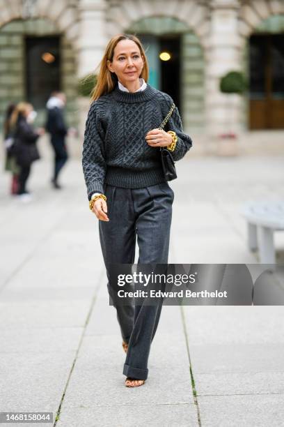 Guest wears a white shirt, a dark gray braided wool pullover, gray suit pants, yellow large bracelets, dark gray large suit pants, beige and brown...