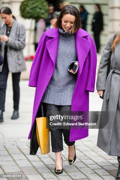 Guest wears a gray wool oversized turtleneck pullover, a purple wool long coat, gray denim pants, a yellow brown shiny leather handbag, black satin...