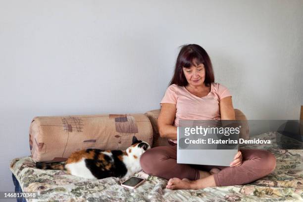 elderly woman working on laptop while sitting on sofa at home - russian business woman stock-fotos und bilder