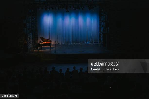 music stage theater with grand piano and white backdrop illuminated with stage light and audience in silhouette - space opera stock pictures, royalty-free photos & images