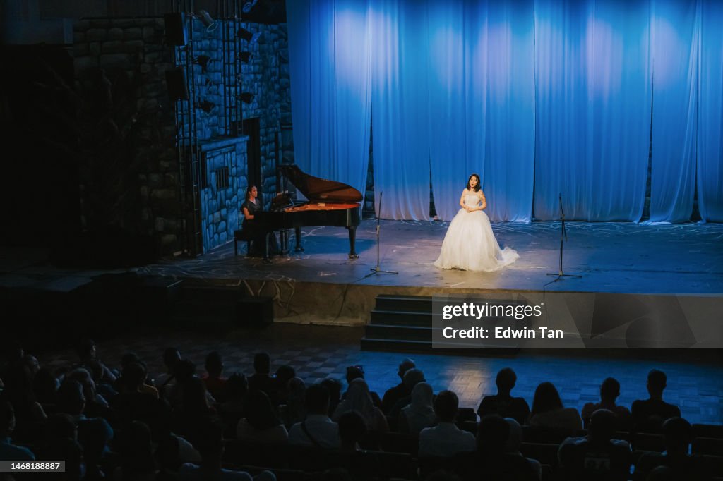 Young Chinese Female opera singer performing solo on stage with Pianist in front of audience