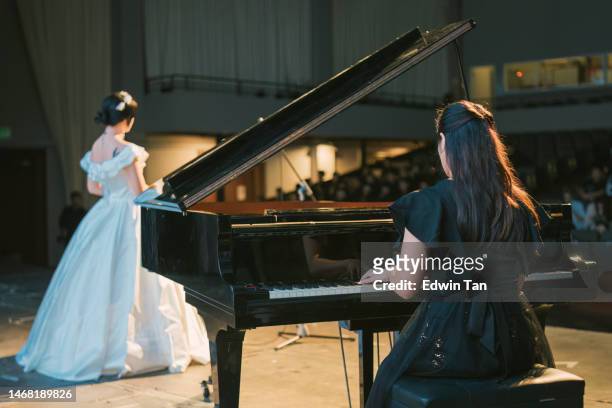 asiatisch-chinesische pianistin spielt flügel mit opernsängerin, die solo auf der bühne steht - chinese opera stock-fotos und bilder