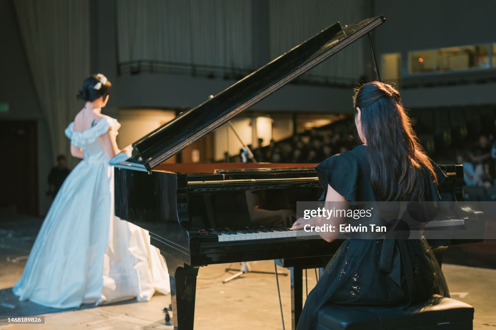 Pianista chino asiático tocando el piano de cola con una cantante de ópera femenina que actúa sola en el escenario