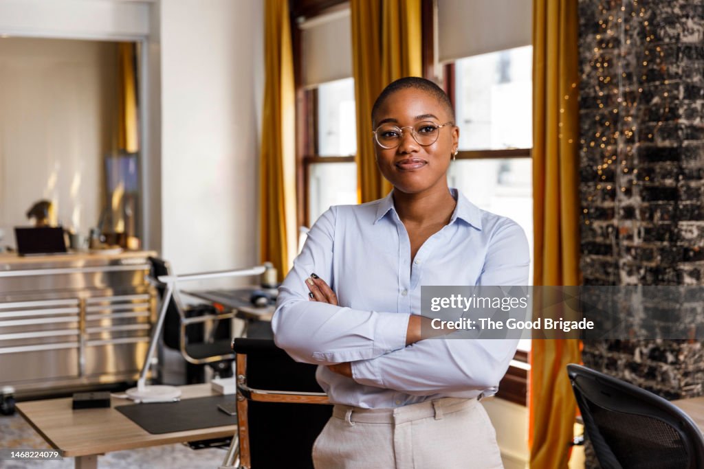 Confident female entrepreneur standing with arms crossed at office