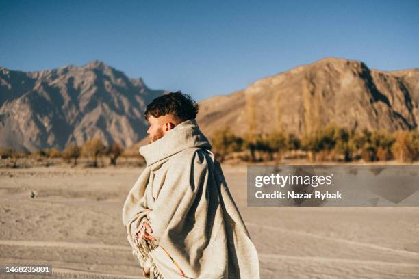 the man wearing in pashtun shawl walking on the sand beach near the indus river in the himalayan mountains - pashtun stock pictures, royalty-free photos & images