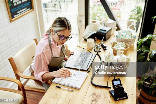 joven propietario de un negocio que usa una computadora portátil en una tienda minorista - pequeña empresa fotografías e imágenes de stock
