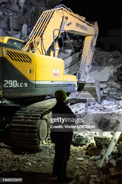 Enfant regardant une pelleteuse déblaysant les gravats de sa maison détruite par le séisme le 9 février 2023 à Alexandrette en Turquie.