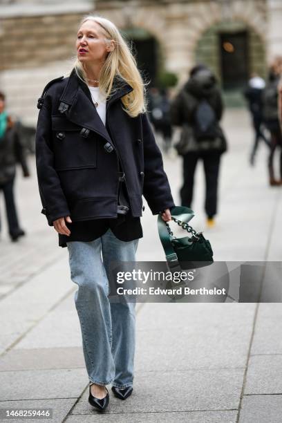 Guest wears gold and diamonds necklace, a gold Trinity necklace from Cartier, a white t-shirt, a black oversized belted jacket, blue faded denim...