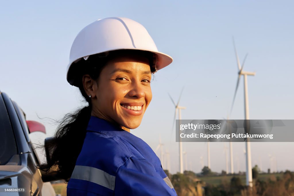Female engineer with electricity producing wind turbines in background.