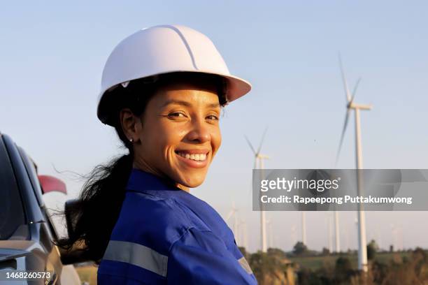 female engineer with electricity producing wind turbines in background. - blue collar portrait stock pictures, royalty-free photos & images