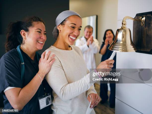 adult woman chemotherapy patient finishing treatment with a ceremonial bell ring - ringing bell stock pictures, royalty-free photos & images
