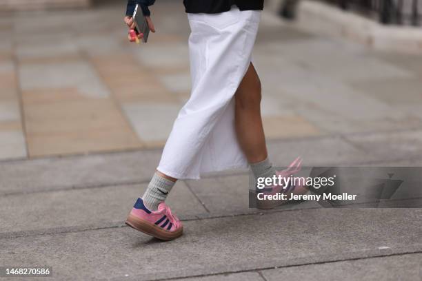 Fashion week guest seen wearing grey navy blue and pink patterned Adidas Gazelle sneakers, grey socks by Nike and a white skirt before the Emilia...