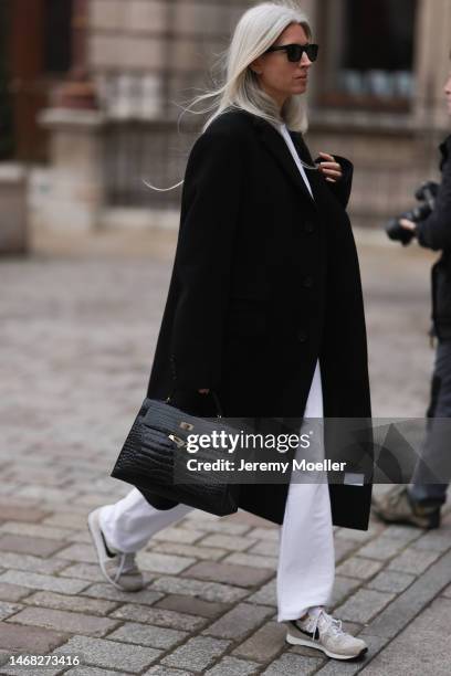 Sarah Harris seen wearing a black Hermes croco Kelly bag, black shades, white pants, a black coat and sneakers before the Emilia Wickstead show...