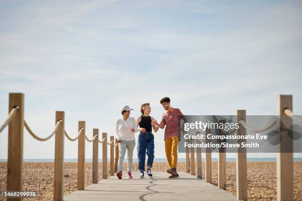 happy friends walking on sunny beach boardwalk - summer fun stock pictures, royalty-free photos & images