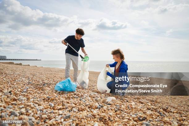 young man and woman collecting garbage on beach - かがむ 人 横 ストックフォトと画像