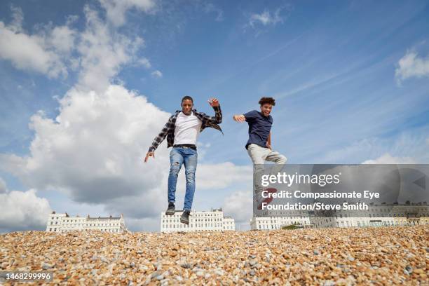 young men jumping on sunny beach - boys jumping stock pictures, royalty-free photos & images