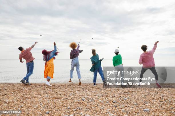 group of friends throwing pebbles into sea - boy throwing stockfoto's en -beelden