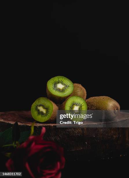 close-up of natural and organic kiwis, on piece of wood, with black background, and red flower, space to copy. - kiwi fruit stock pictures, royalty-free photos & images