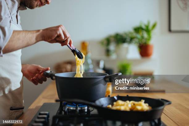 un hombre anónimo cocinando pasta en la cocina - sartén fotografías e imágenes de stock