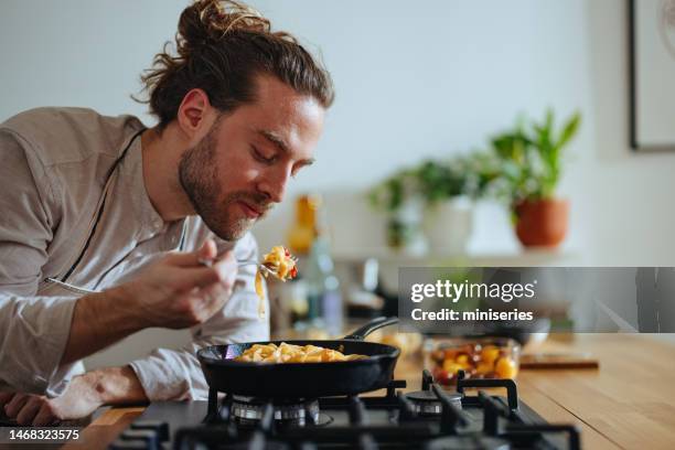 lächelnder koch probiert pasta mit frischem gemüse - one pot pasta stock-fotos und bilder