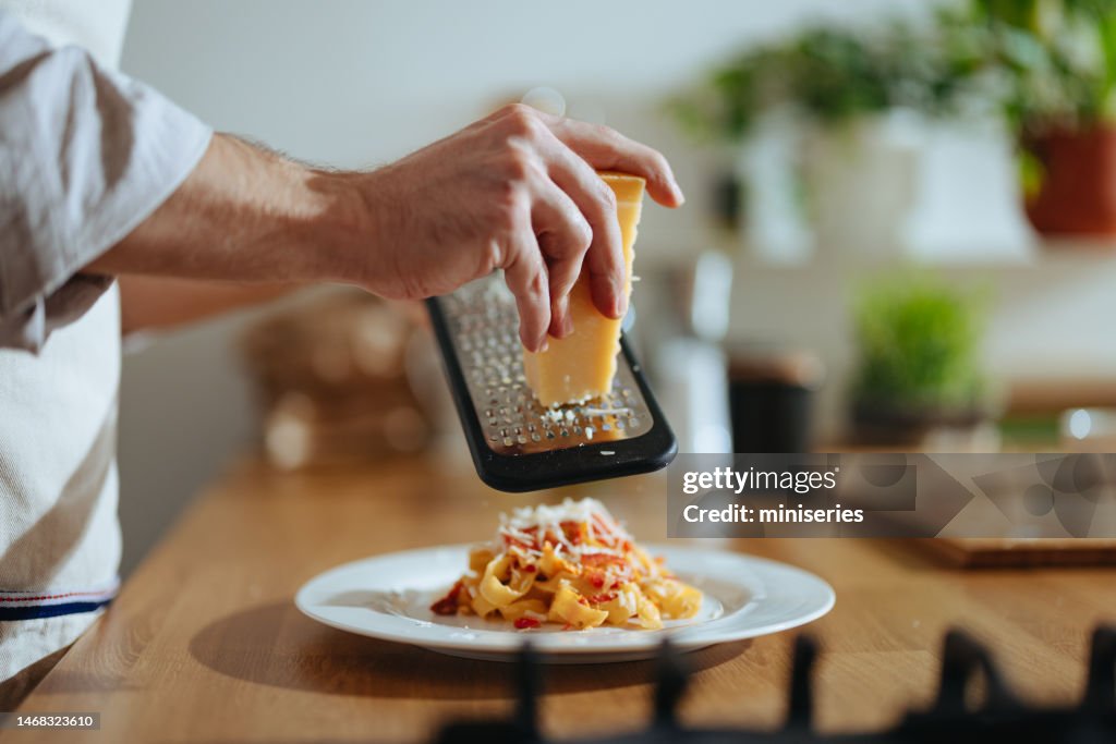 Close Up Photo Of Man’s Hands Grating Cheese Into Pasta With Fresh Vegetables