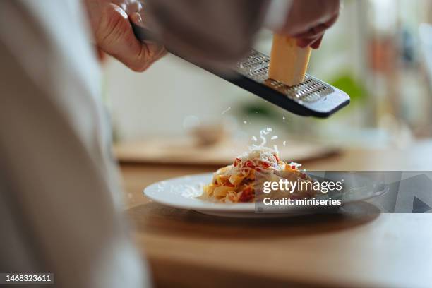 nahaufnahme foto von männerhänden, die käse in nudeln mit frischem gemüse reiben - parmesan stock-fotos und bilder