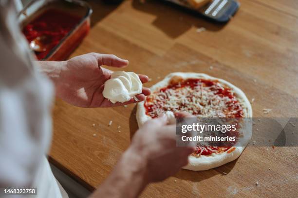 close up photo of man’s hands putting mozzarella cheese on a pizza - mozzarella stock pictures, royalty-free photos & images