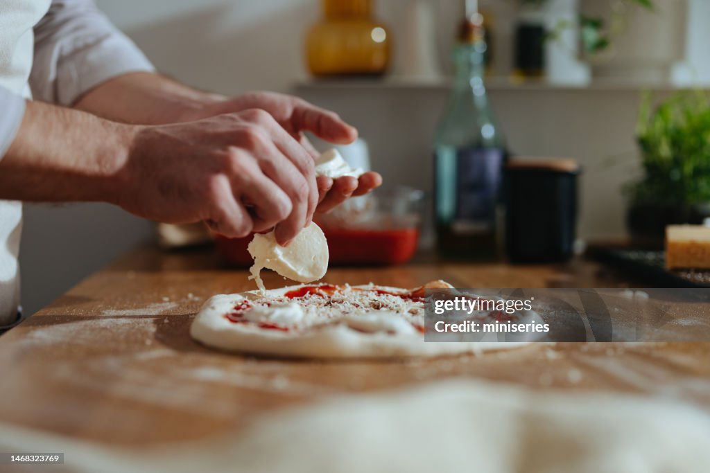 Nahaufnahme Foto von Männerhänden, die Mozzarella-Käse auf eine Pizza legen