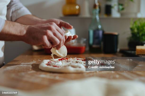 foto de cerca de las manos de un hombre poniendo queso mozzarella en una pizza - mozzarella fotografías e imágenes de stock