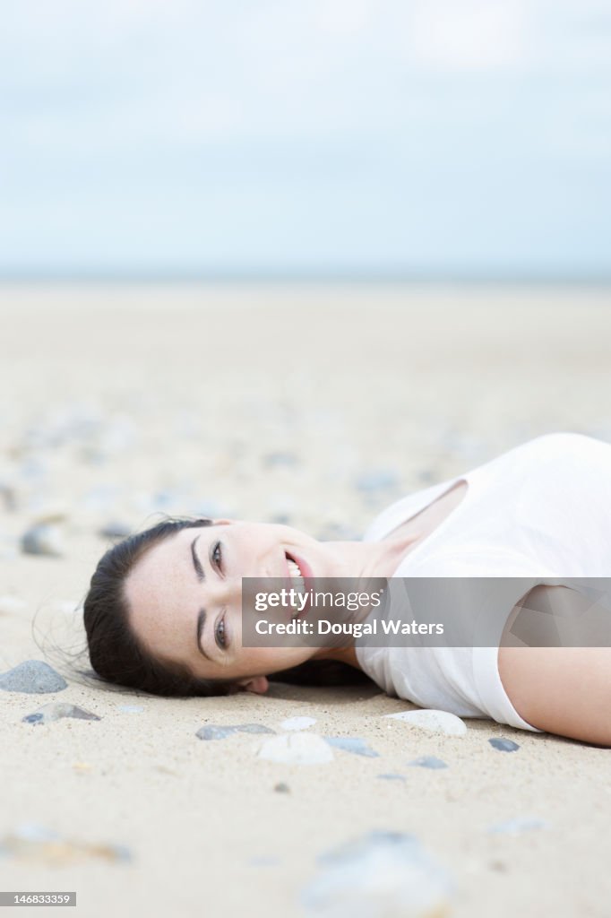 Woman laying on beach smiling.