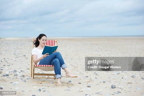 woman  sitting at beach reading book. - man on the beach relaxing in deckchair stock-fotos und bilder