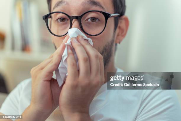 young man with a cold, blowing his nose with a piece of tissue paper - covering nose stock pictures, royalty-free photos & images