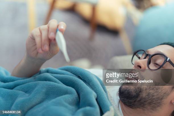 young man with high fever, taking his temperature with a thermometer. - altitude sickness stock pictures, royalty-free photos & images