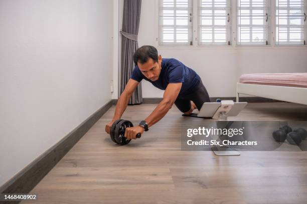 asian man doing to strength training and body core exercises with abdominal toning wheel at home - training wheels imagens e fotografias de stock