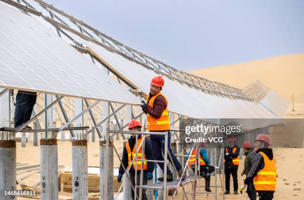 Workers install solar panels at the construction site of a 100MW solar photovoltaic power project, which is also used to promote desert ecological...