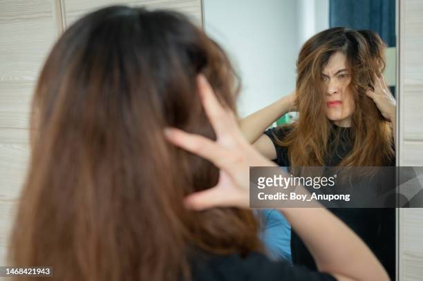 unhappiness asian woman having stress after she saw her messy and tangled hair in the mirror after waking up in the morning. - frizzy fotografías e imágenes de stock