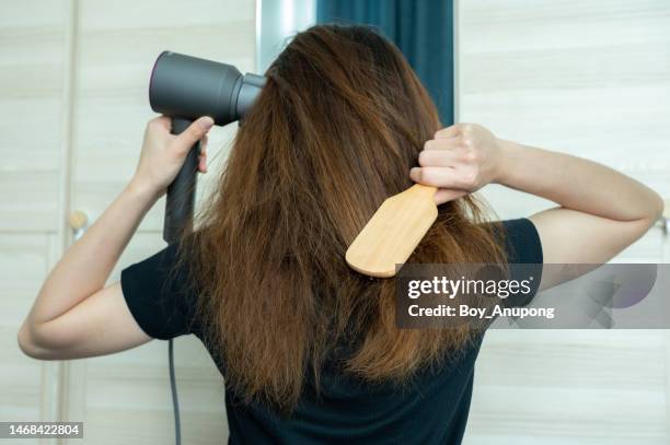 rear view of young asian woman using a comb for brushing her hair with a hair dryer for blowing water to dry her hair. - brushed back hair stock pictures, royalty-free photos & images