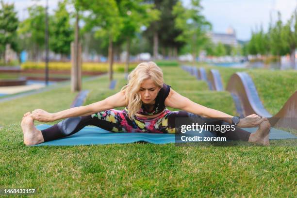 mid adult woman practicing yoga in seated wide legged straddle pose, springtime in the park - straddle split stock pictures, royalty-free photos & images