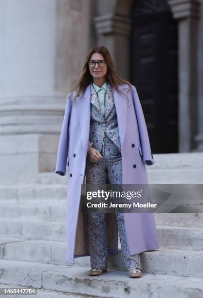 Fashion week guest seen wearing a long purple coat, a matching flower printed suit with a blazer and pants, a blouse and beige ballet flats before...
