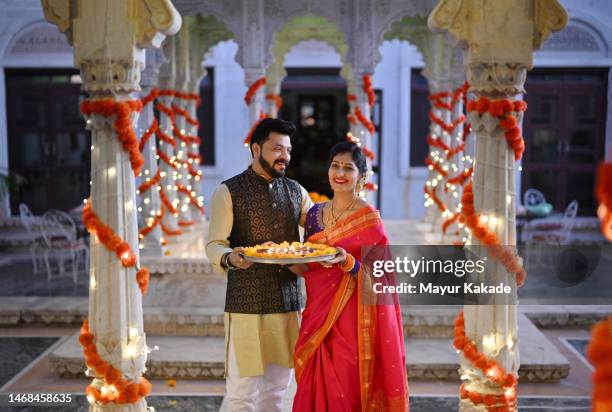 mid adult couple in traditional festive wear holding a plate of oil lamps (diya) in the marble pavilion of a palace during a traditional festival - arranging stock pictures, royalty-free photos & images