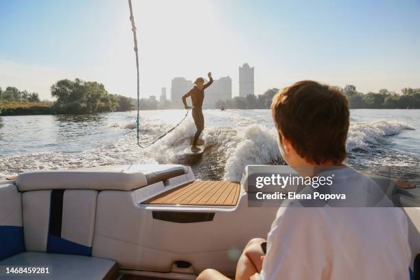 silhouette adult female surfer wakeboarding with surfboard leash behind speedboat on sunrise moment - モーターボートに乗る ストックフォトと画像