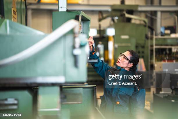 asian female factory worker operating an industrial machine - construction equipment stockfoto's en -beelden