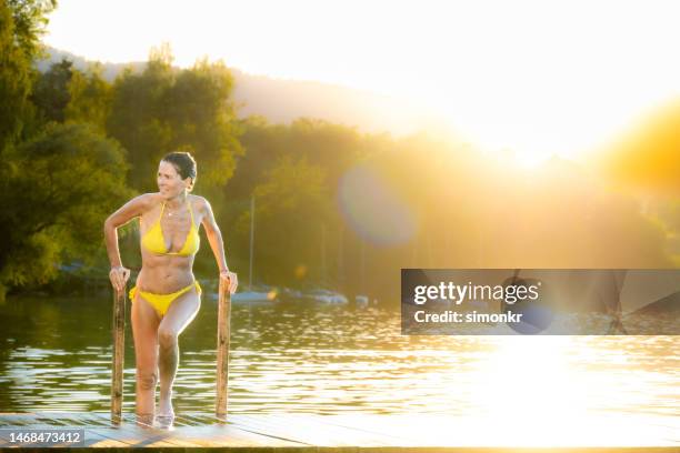 woman in yellow bikini by lake - older woman wet hair stock pictures, royalty-free photos & images