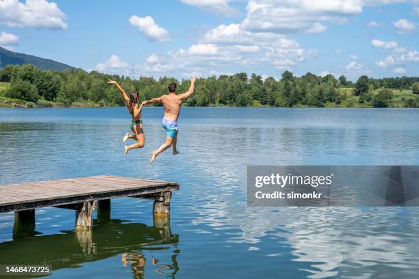 young couple jumping in lake - group-of-friends-jumping-off-dock-into-lake stock pictures, royalty-free photos & images