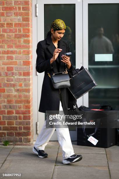 Guest wears gold embroidered rhinestones on the hair, a black long coat, a black shiny leather crossbody bag , a black shopping bag, white large...